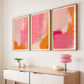Three abstract art pieces in pink and orange frames on a wall above a console table.