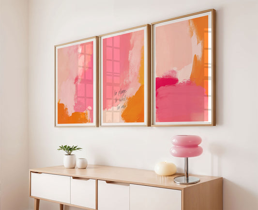 Three abstract art pieces in pink and orange frames on a wall above a console table.