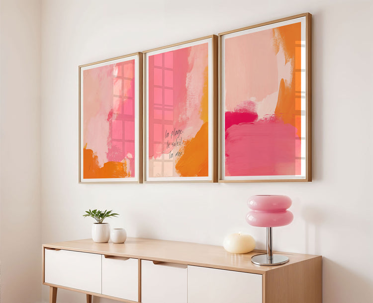 Three abstract art pieces in pink and orange frames on a wall above a console table.