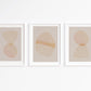 Three abstract art prints with geometric shapes in soft colors on a white wall.